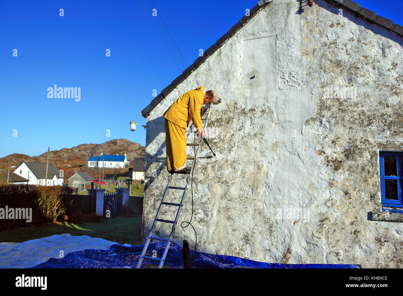 Mann mit einem Hochdruckreiniger Lack von der Giebelseite ein Cottage zu Streifen Stockfoto