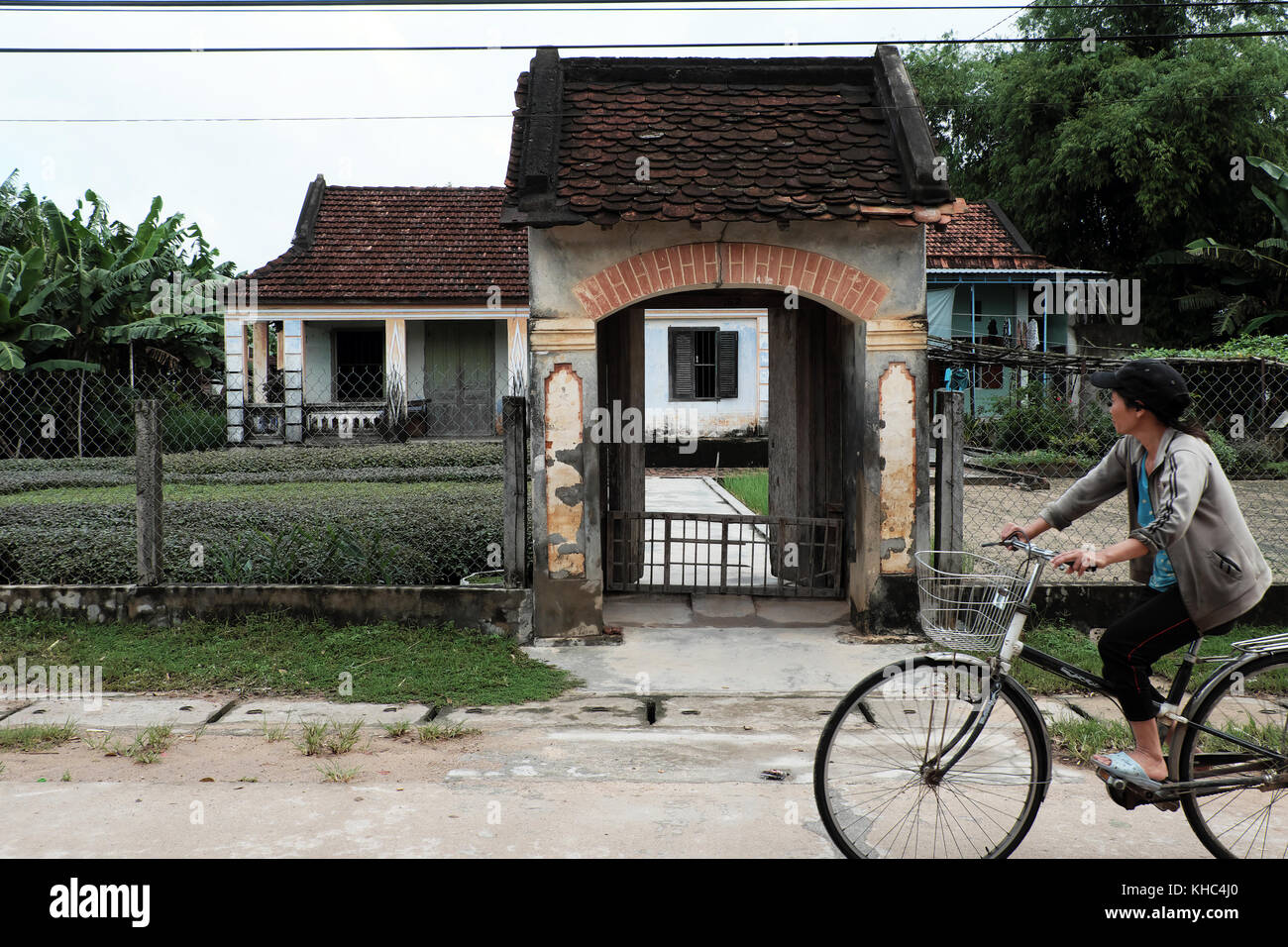 Vietnamesisches altes Haus mit Holztür, Holzfenster und erstaunlichem großen Betontor, Frau fährt Fahrrad und sieht altes Zuhause aus Stockfoto