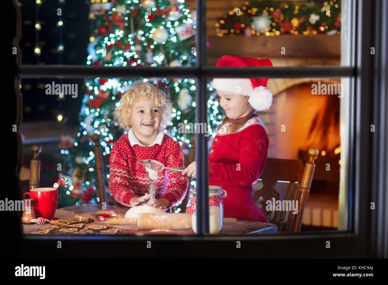 Kinder backen Weihnachtsplätzchen am Kamin und geschmückten Baum