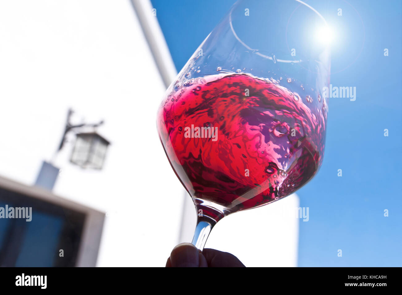 Hand mit Glas Rotwein, wirbelnden und Bewertung im sonnigen blauen Himmel im Freien im Freien Weinprobe Terrasse Lage Stockfoto