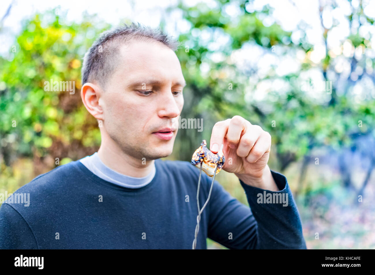 Junger Mann peeling verkohlte Haut auf gerösteten karamelisierten Marshmallow Spieß Closeup Portrait Stockfoto