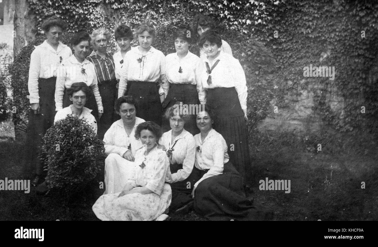 Ein Foto von dreizehn Frauen, die für ein Foto posieren, elf der Frauen scheinen in einer Uniform zu sein, die aus einem schwarzen Rock in voller Länge und einem weißen langärmeligen Oberteil besteht, sie posieren in einem Gartenbereich mit Efeu, der hinter ihnen die Wand klettert, Morrisania, Bronx, New York, 1900. Aus der New York Public Library. Stockfoto