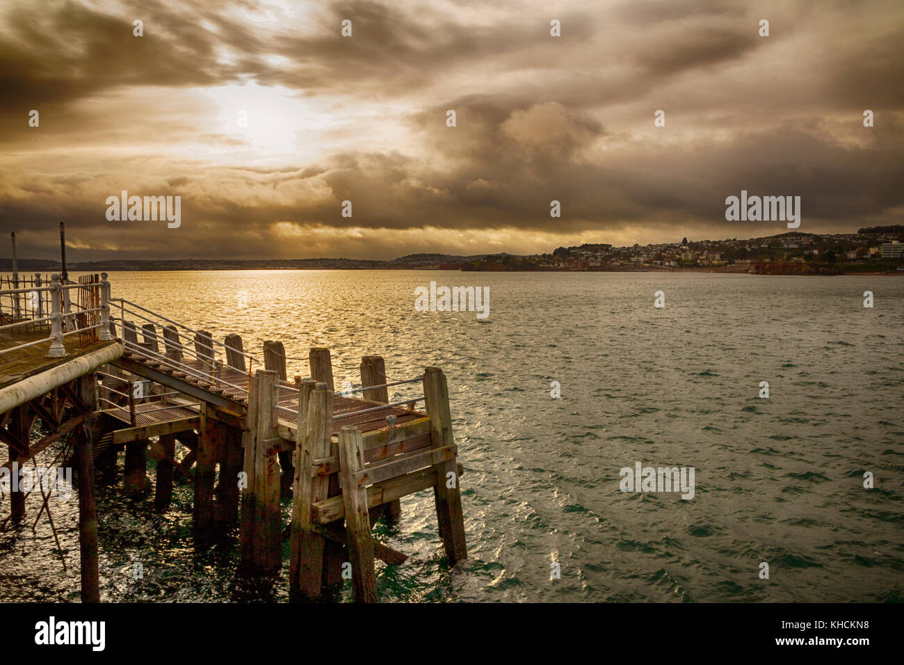 Sonnenuntergang über Torbay von Torquay Pier mit einem Bootssteg im Vordergrund. Dunkle Wolken mit Sturm nähert. Stockfoto