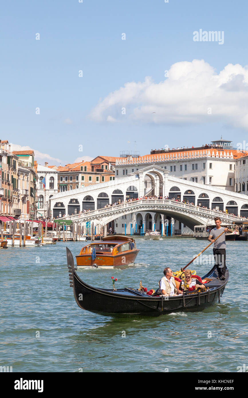 Gondoliere Rudern eine touristische Paar in seiner Gondel vor der Rialto Brücke, Venedig, Italien mit einem Wassertaxi vorbei Stockfoto