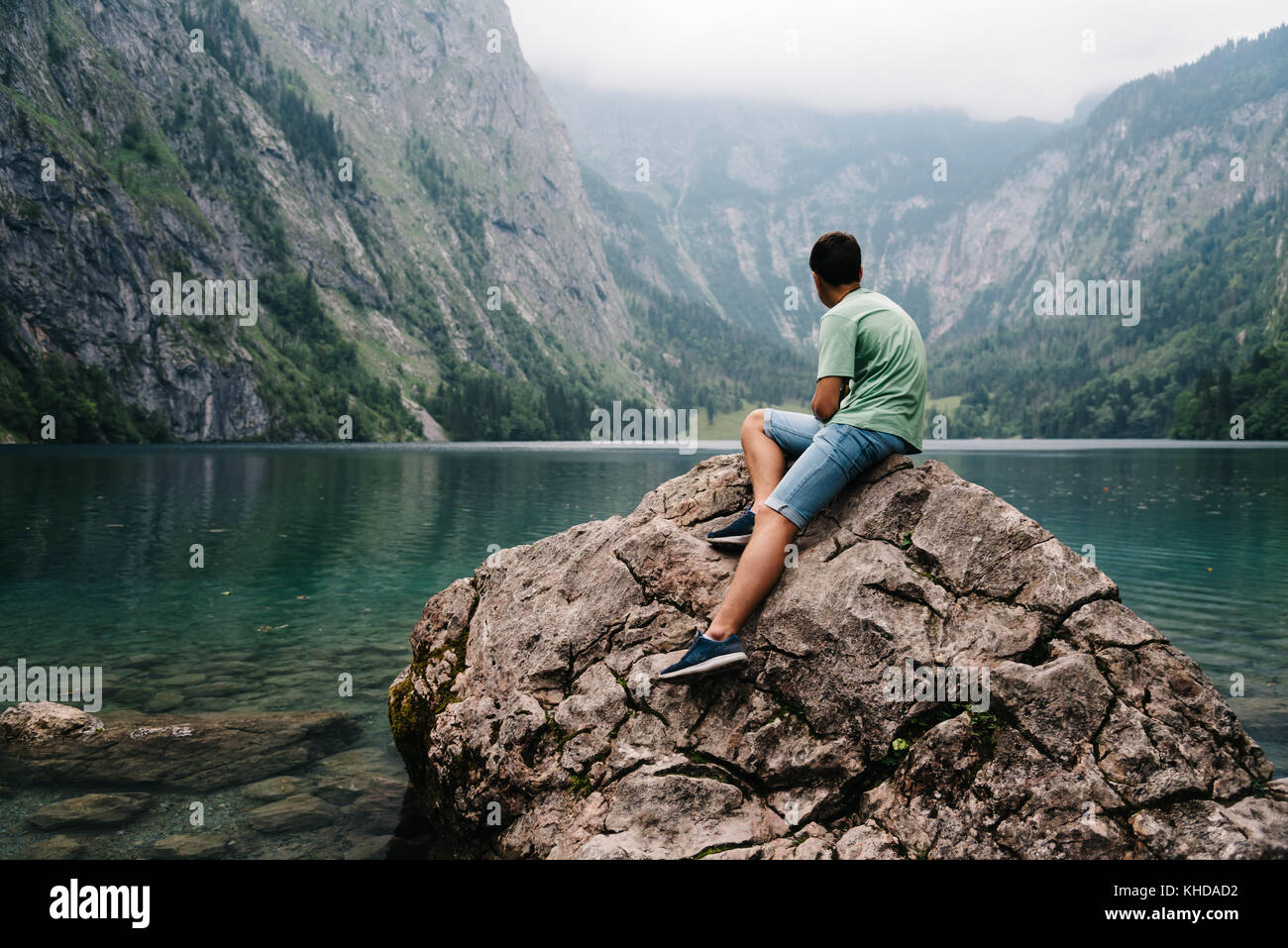 Junger Erwachsener Mann sitzt auf Felsen an schönen und Misty l suchen Stockfoto