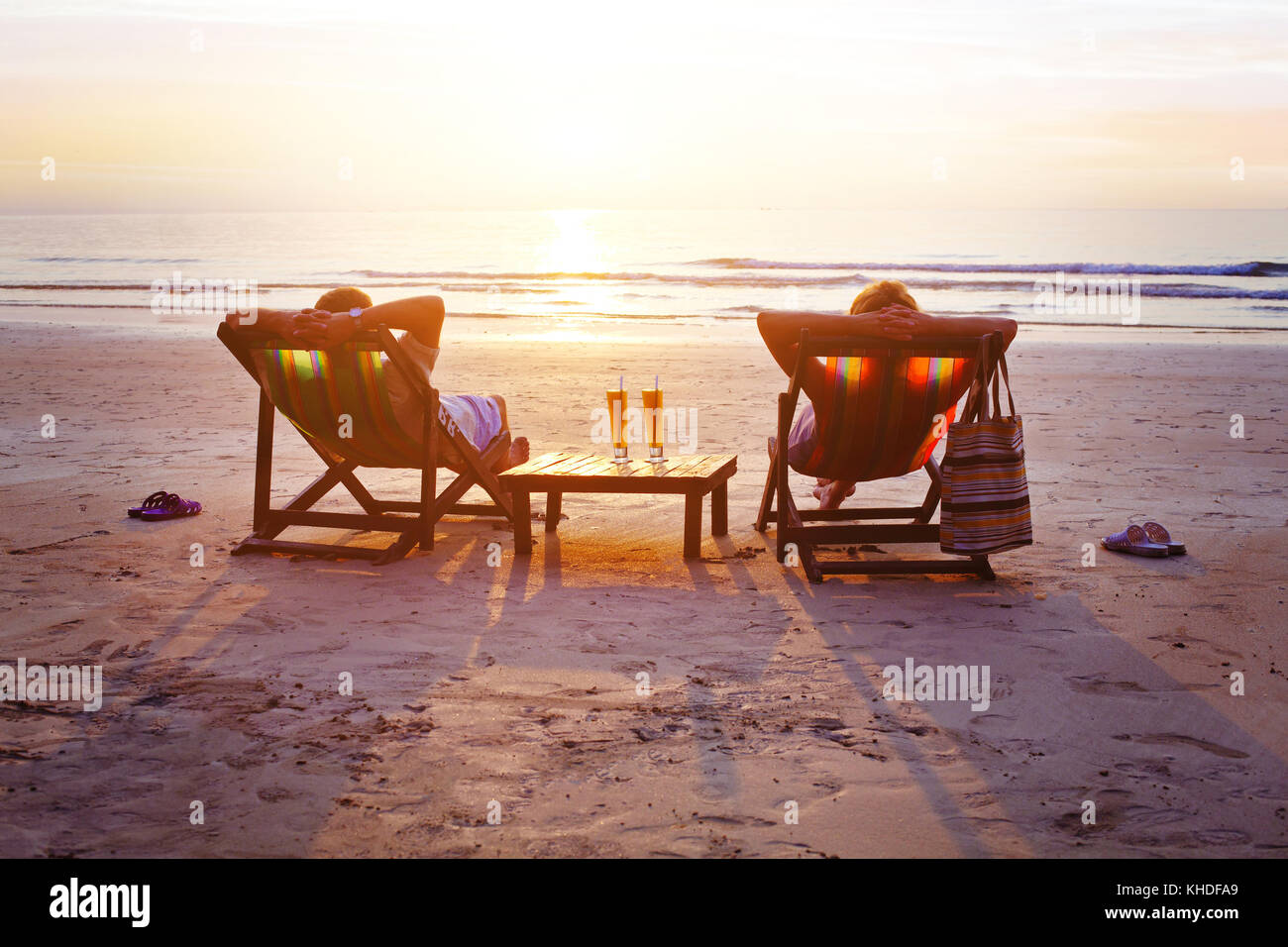 Flitterwochen reisen, Silhouetten von glückliches Paar entspannen in Liegestühlen am Strand bei Sonnenuntergang Stockfoto