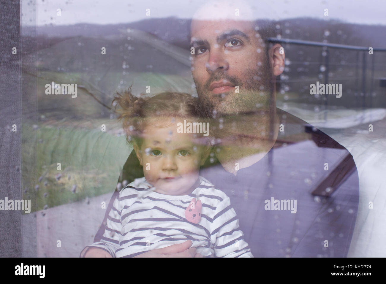 Mann mit Kind auf der Suche durch das Fenster beobachten Regen fallen Stockfoto