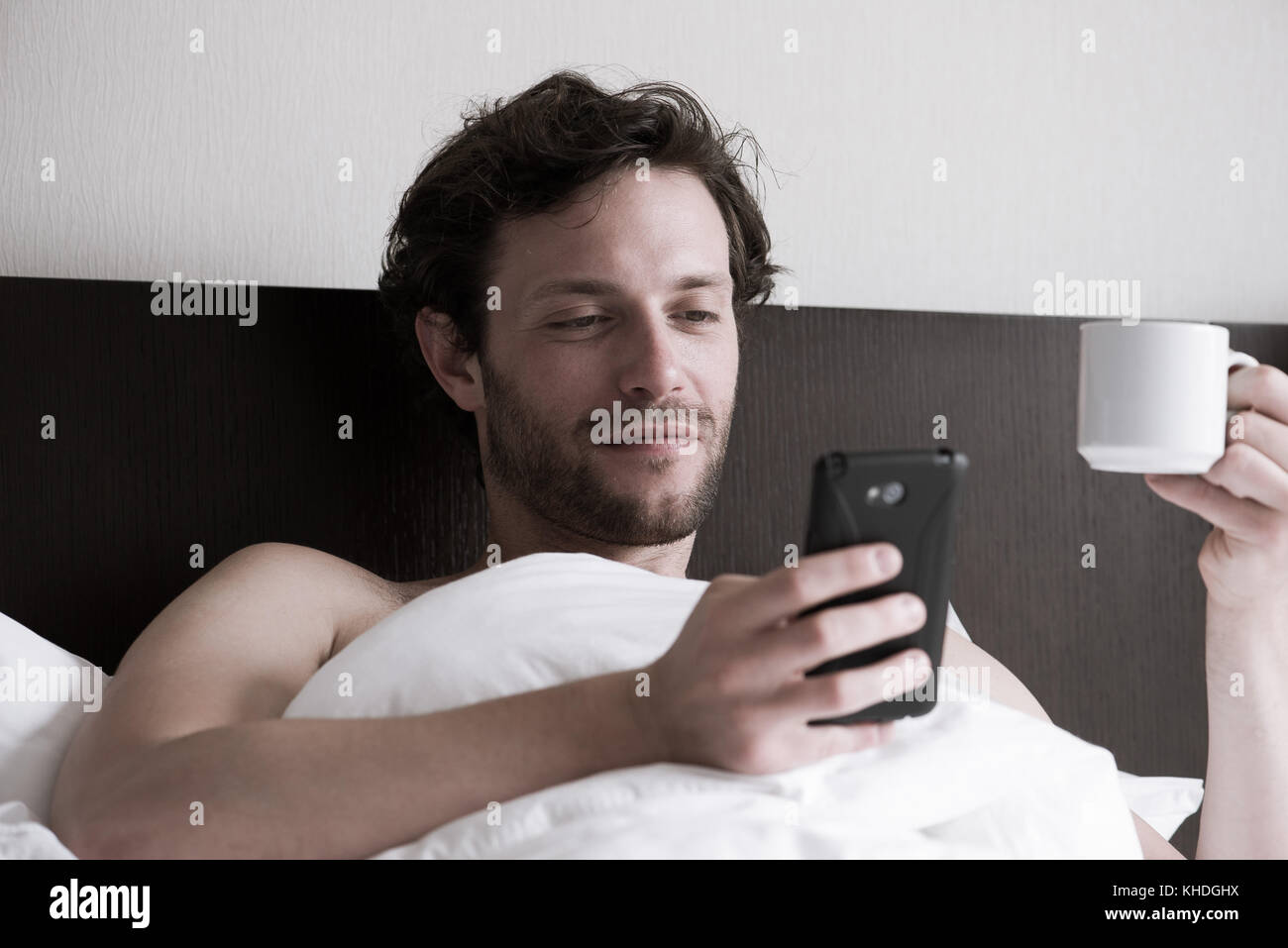 Mann im Bett mit Smartphone und trinken heißen Getränk Stockfoto