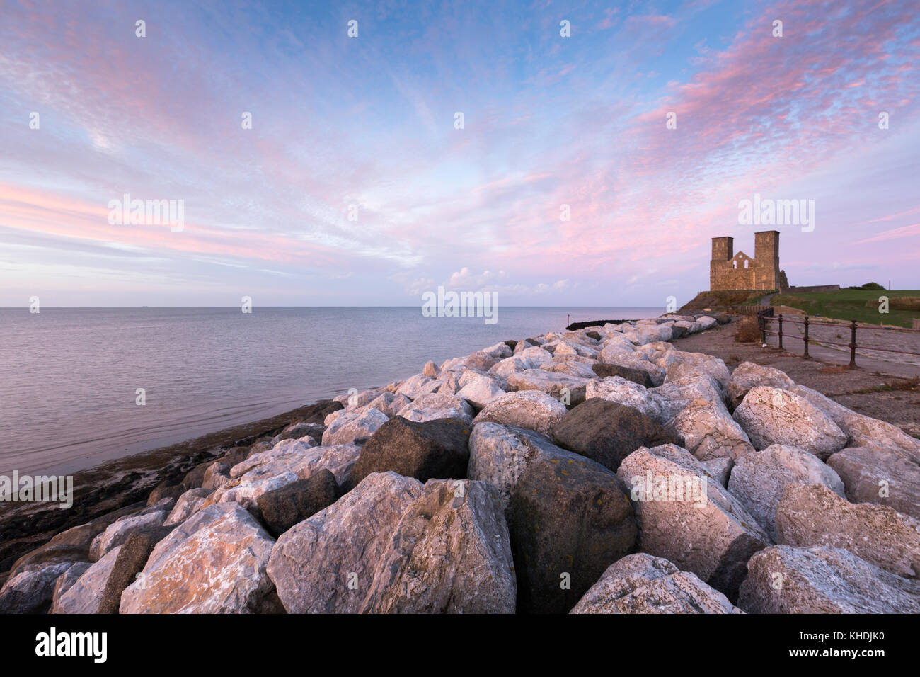 Ein lebendiges rosa Sonnenuntergang an Reculver Towers, die Mittelalterliche Kirche an Reculver auf der nördlichen Küste von Kent, UK. Die Felsen im Vordergrund sind Meer Verteidigung. Stockfoto