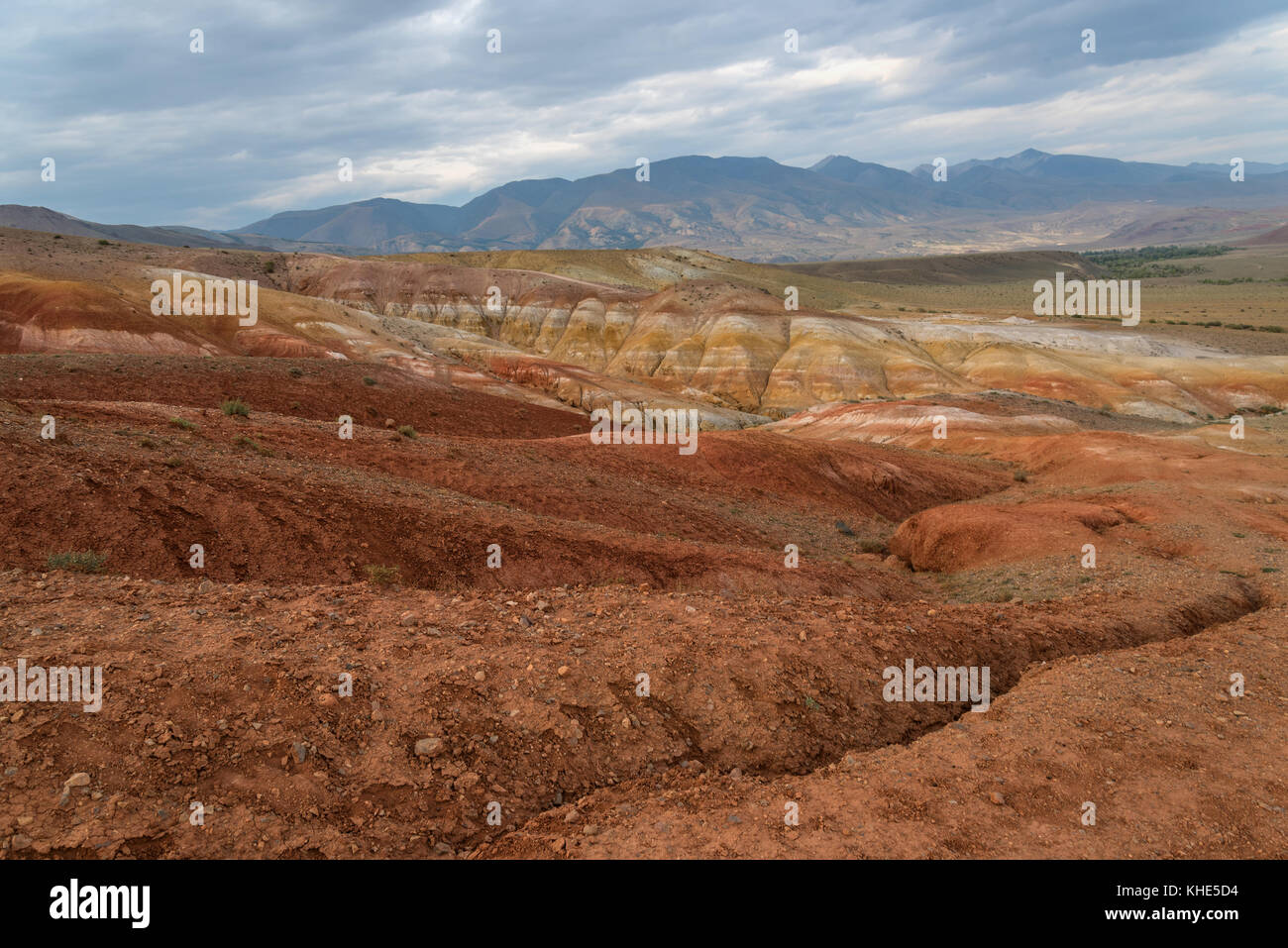 Malerischen Steppe, Wüste Landschaft mit bunten Berge, Risse im Boden und spärliche Vegetation auf dem Hintergrund der bewölkten Himmel Stockfoto