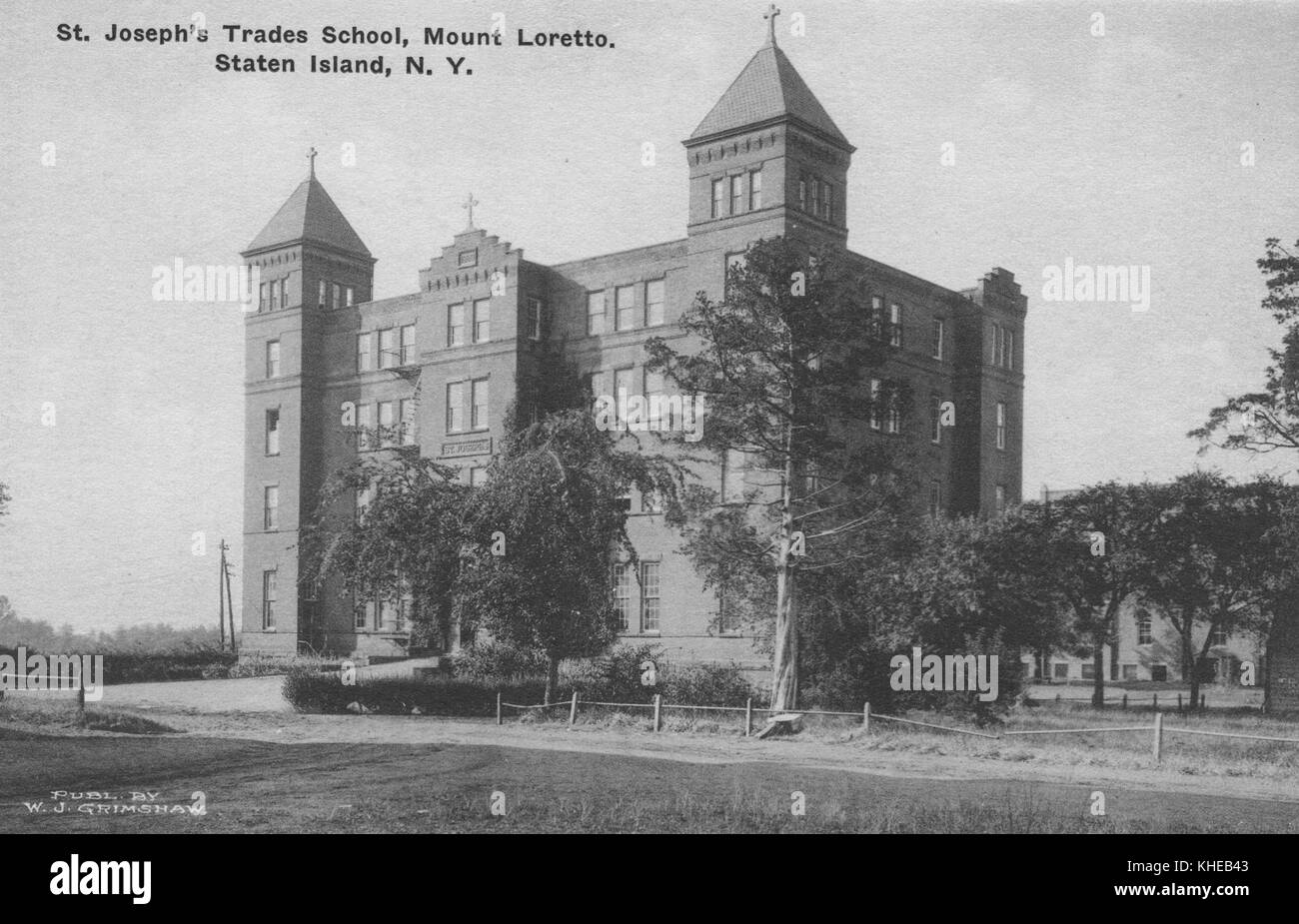 Ein altes Postkartenbild des St. Joseph's Trade School Gebäudes, Eckansicht der Vorderseite und der linken Seite, mit mehreren Bäumen und Gras im Vordergrund, Mount Loretto, Staten Island, New York, 1900. Aus der New York Public Library. Stockfoto