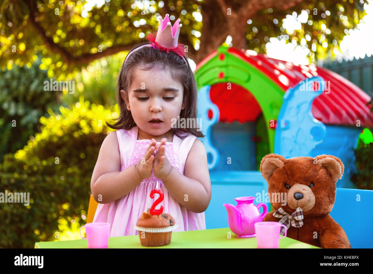 Baby Kleinkind Mädchen im Freien zweiten Geburtstag händeklatschen am Kuchen mit Teddy Bär als bester Freund, Playhouse und Kaffee. rosa Kleid und Krone. Stockfoto