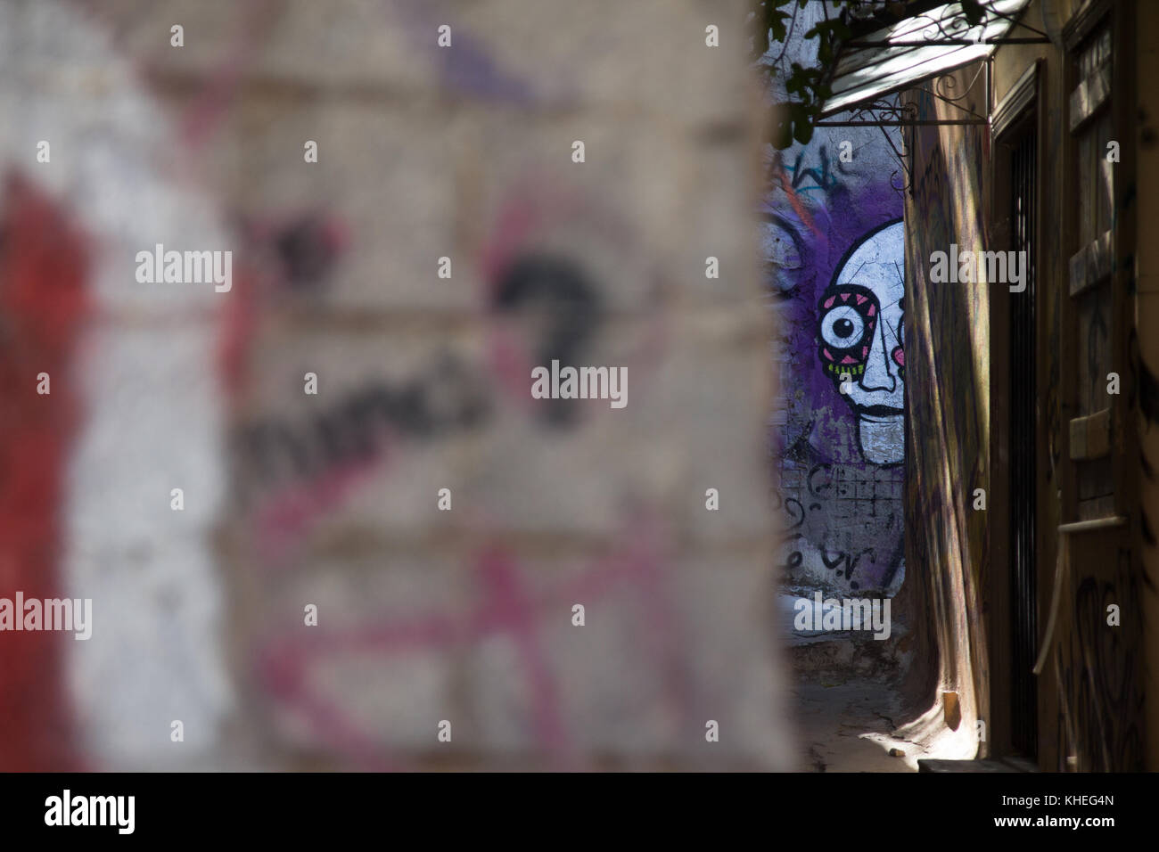 Graffiti eines gruseligen Gesichts durch eine Öffnung in einer kleinen Straße in der Plaka-Region in Athen, Griechenland Stockfoto