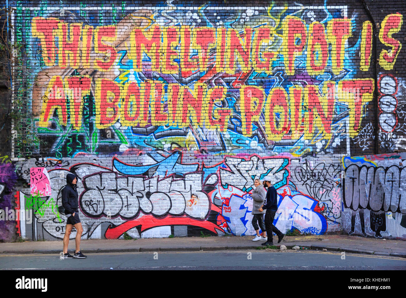 Menschen zu Fuß Vergangenheit grafitti Street Art sloagan "Dieser Schmelztiegel ist am Siedepunkt" mit sozialen Kommentar in Shoreditch, London, UK Stockfoto