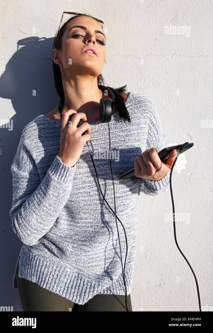 Junge trendige Urban Hipster Frau mit Kopfhörer und Tablet an Wand posieren, im Freien Stockfoto