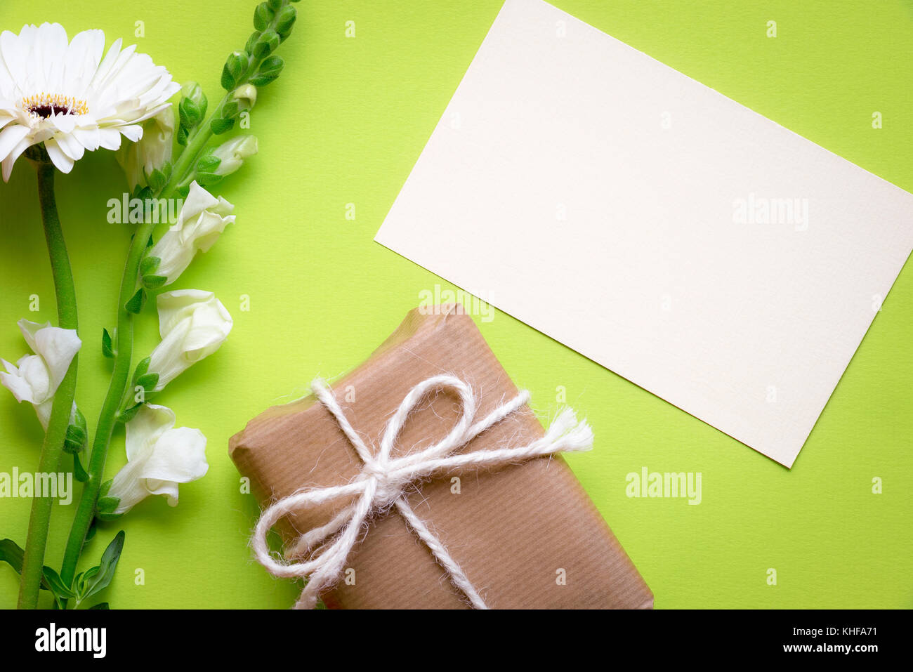 Grußkarte Idee mit einem Papier Hinweis von weißen Blüten und einem Geschenkkarton in braunem Papier eingewickelt umgeben und gebunden mit Flachs string und Bogen, auf einem grünen b Stockfoto