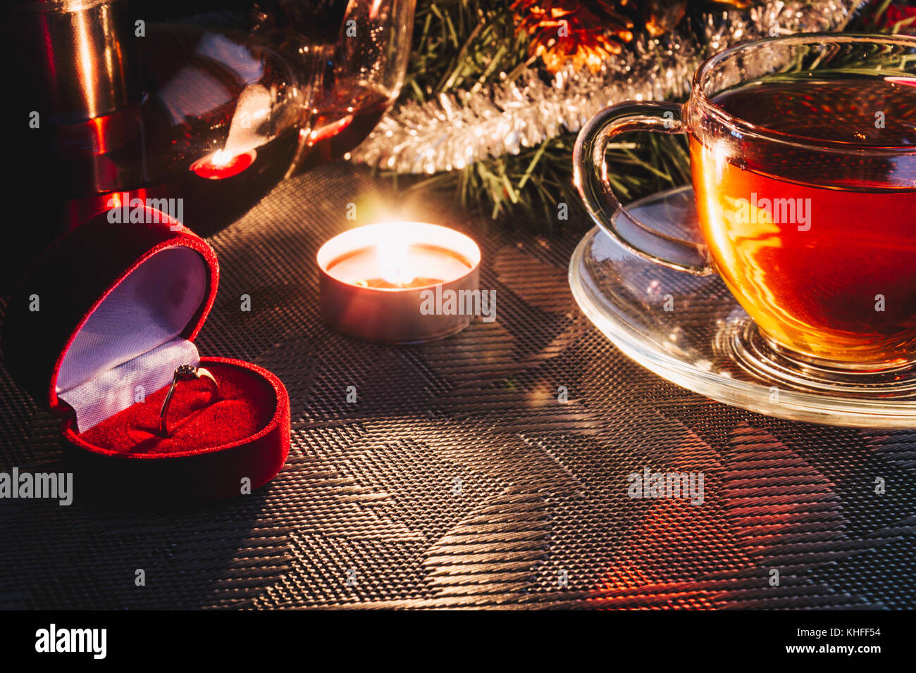 Engagement Ring in Velvet Red Box auf dem Tisch in der Nähe von Weihnachtsschmuck, Tasse warmen Tee und Kerze. Hochzeit Vorschlag an Heiligabend. Stockfoto