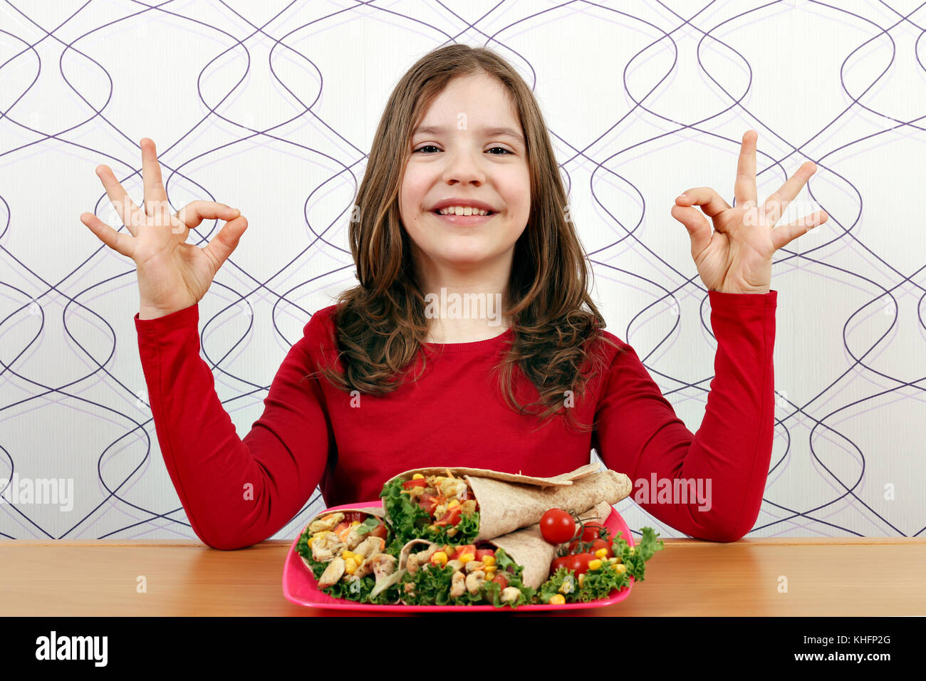 Glückliche kleine Mädchen mit Burritos und ok Handzeichen Stockfoto