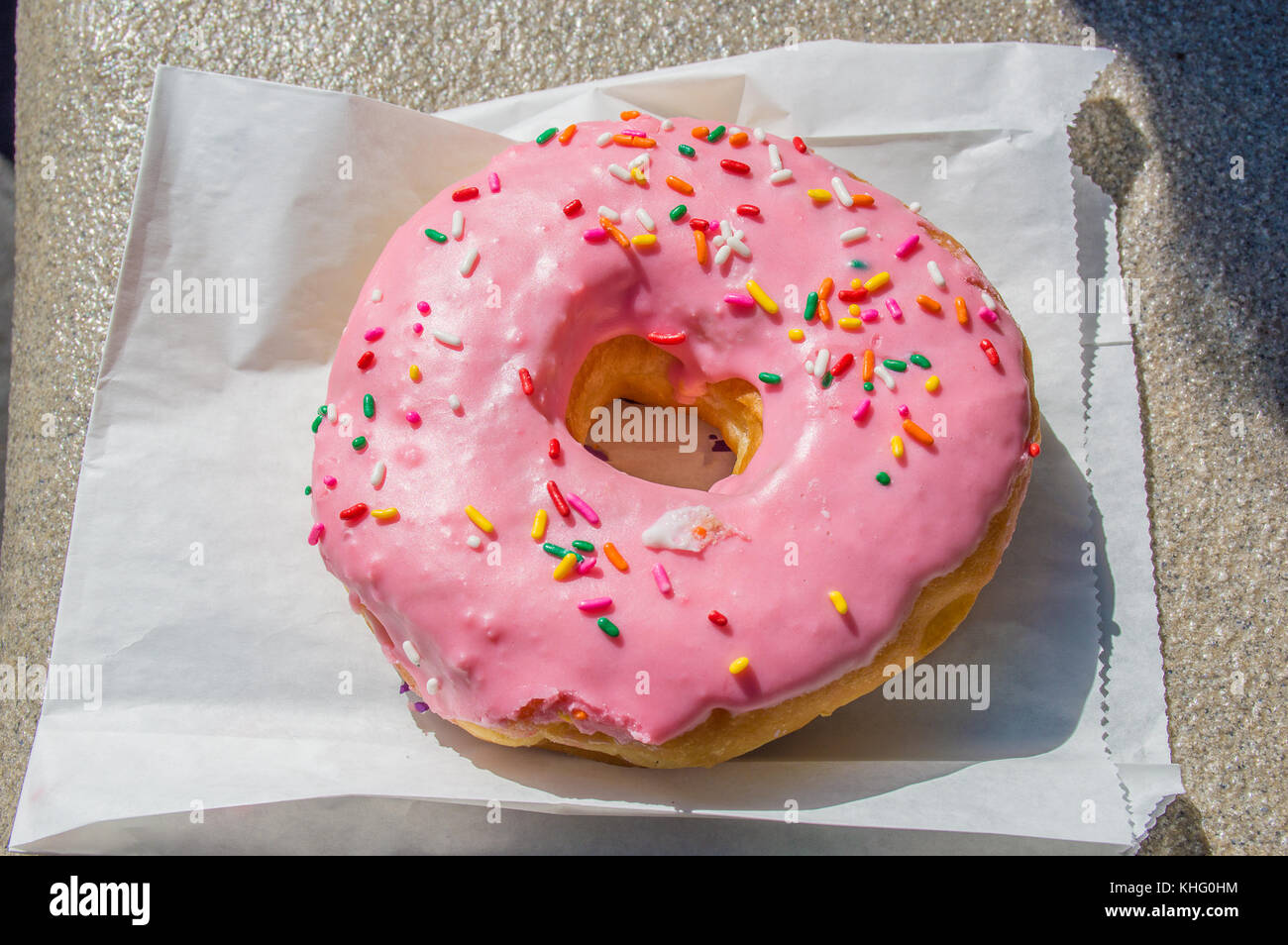 Große rosa iced Donut auf eine Papiertüte Stockfoto