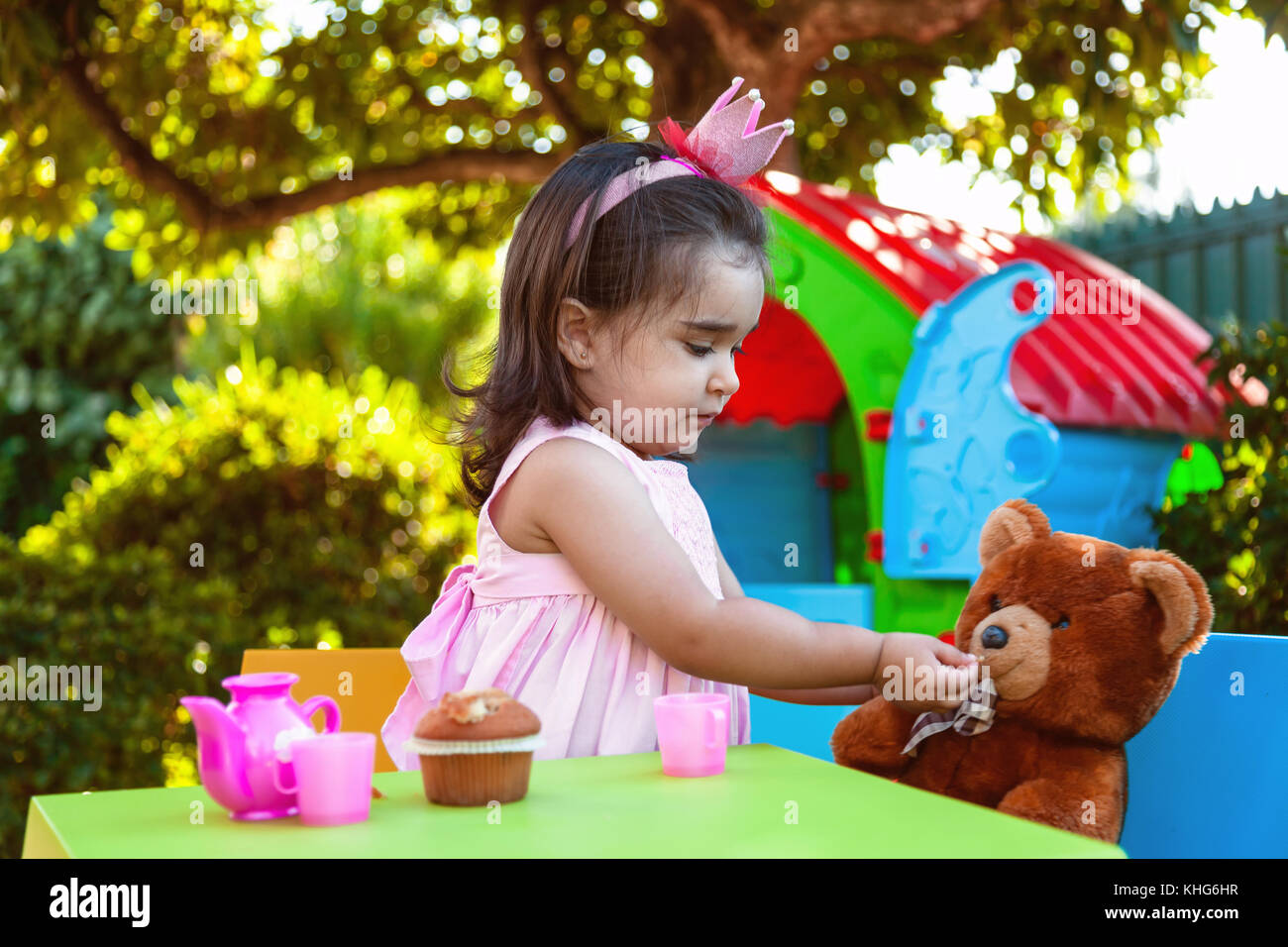 Baby Kleinkind Mädchen spielen Im freien Tea Party Fütterung ihr bester Freund Teddy Bear mit Süßigkeiten Gummibärchen. rosa Kleid und Königin oder Prinzessin Krone. Stockfoto