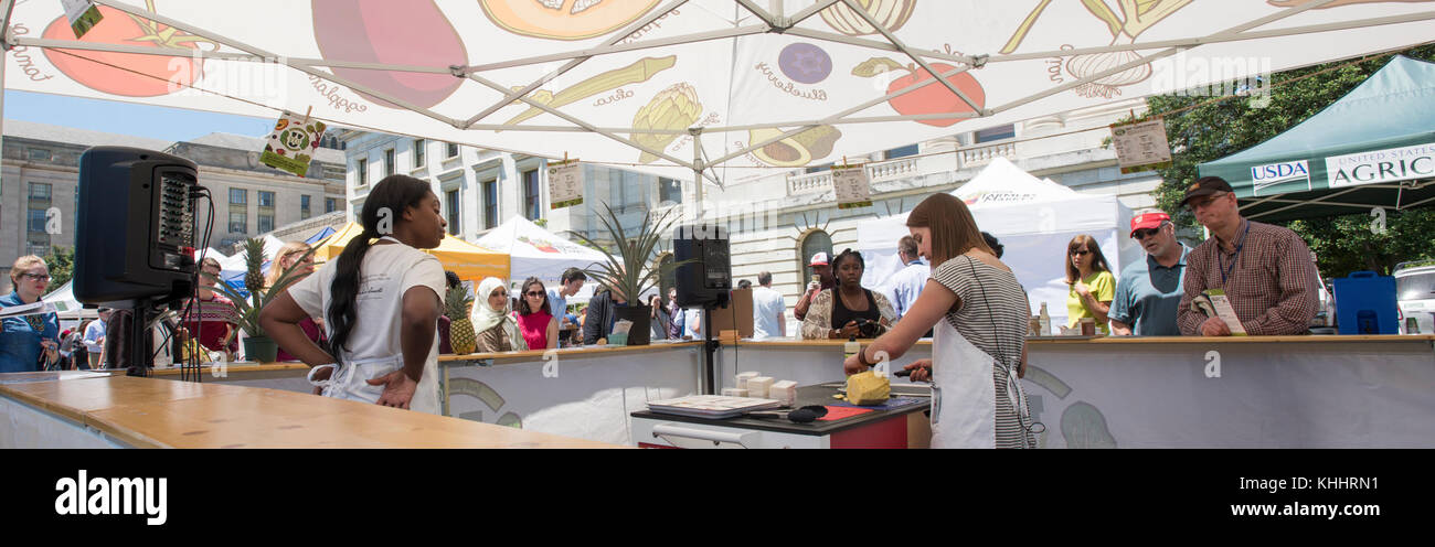 „VegU“-Programmkoordinatorin Laura Popielski bietet sichere Ananas-Schneide-Praktiken und Lagertipps an, und Kayla Johnson liefert am 9. Juni 2017 im „VegU(cation)“-Zelt des USDA Farmers Market in Washington, D.C., Anbauinformationen und Auswahltipps. Gemüsepädagogen oder „VegUcators“ führen kostenlose 10-minütige Obst- und Gemüsekurse durch. Ihre geplanten Demonstrationstermine sind die höchste Erntezeit, um diese Lebensmittel auf den Märkten zu suchen. Das Ziel ist es, Obst und Gemüse in den Mahlzeiten zu erhöhen und den Menschen zu helfen, zu verstehen, wha Stockfoto