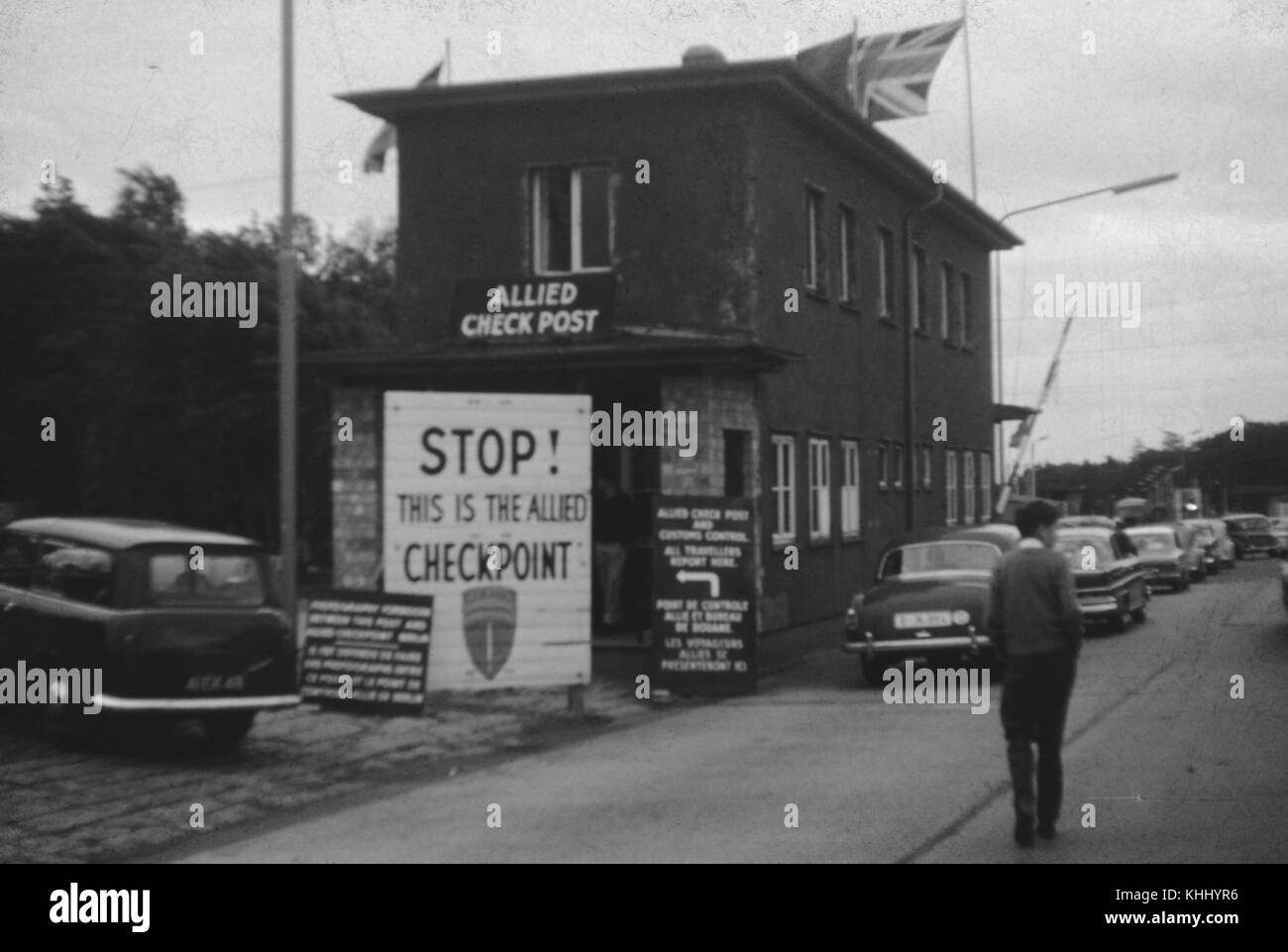 Mann mit den Händen in den Taschen zu Fuß in Richtung eine alliierte Checkpoint zwischen Ost-Berlin und West-berlin, mit Top ist ein Zeichen lesen, dies ist die Allied Checkpoint" und eine Reihe von Autos warten die Grenze, Deutschland, 1961. Stockfoto