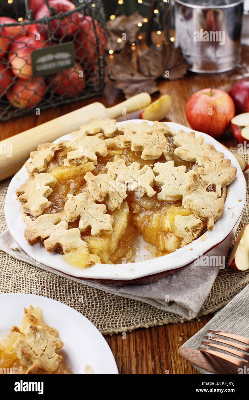 Frisch gebackenen Apfelkuchen mit oberen Kruste in autumn leaves Form und Stück fehlt. die Äpfel im Hintergrund. Stockfoto