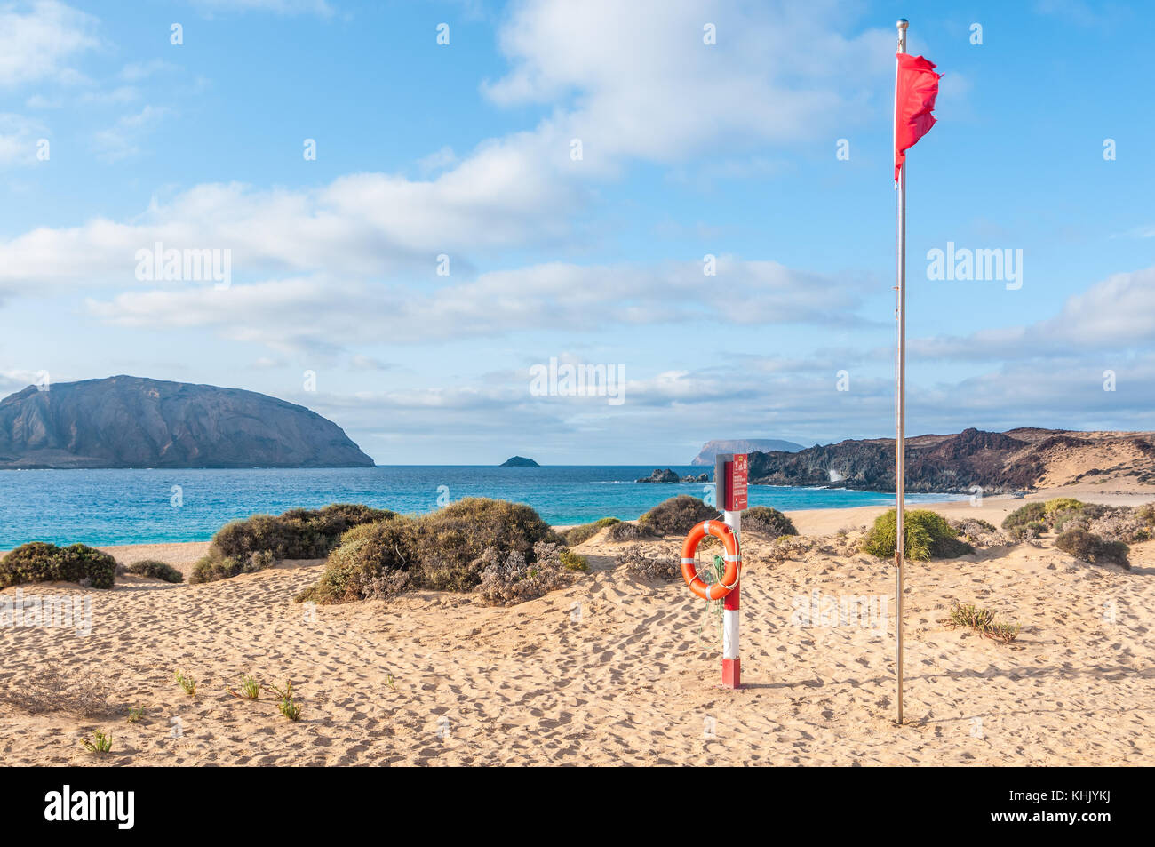 Blick auf Playa de las Conchas mit Montaña Clara Insel im Hintergrund auf der linken Seite und Roque del Infierno auf der rechten Seite mit der roten Flagge und lebensretter ich Stockfoto
