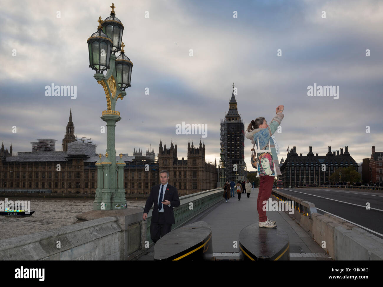 Mit der Winterlandschaft von Westminster und die Häuser des Parlaments auf der Themse gegenüber, eine Frau mit einem David Bowie Tasche steht auf den Anti-terror-Sicherheit Sperren am südlichen Ende der Westminster Bridge, um ein Bild von dem London Eye, am 8. November 2017, in Lambeth, London. Stockfoto