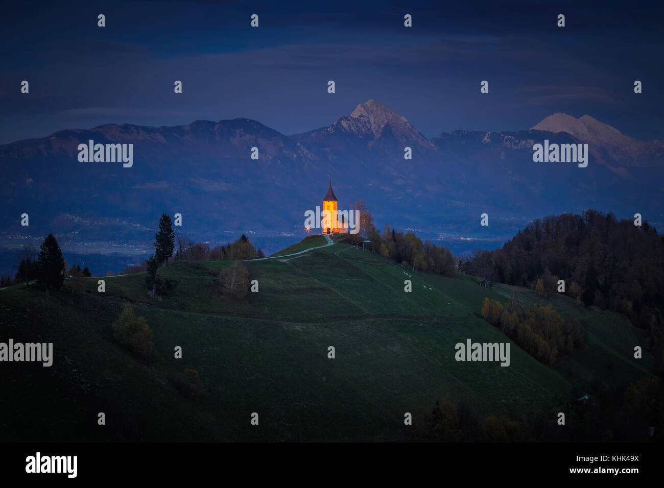 Jamnik, Slowenien - Blaue Stunde in Jamnik mit beleuchteter St. Primoz-Kirche. Julian Alpen im Hintergrund Stockfoto