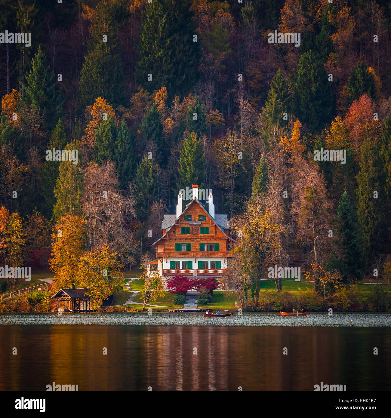 Bled, Slowenien - Typisches slowenisches alpen-haus am Bleder See mit Booten und schönem farbenfrohen Herbstwald bei Sonnenuntergang Stockfoto