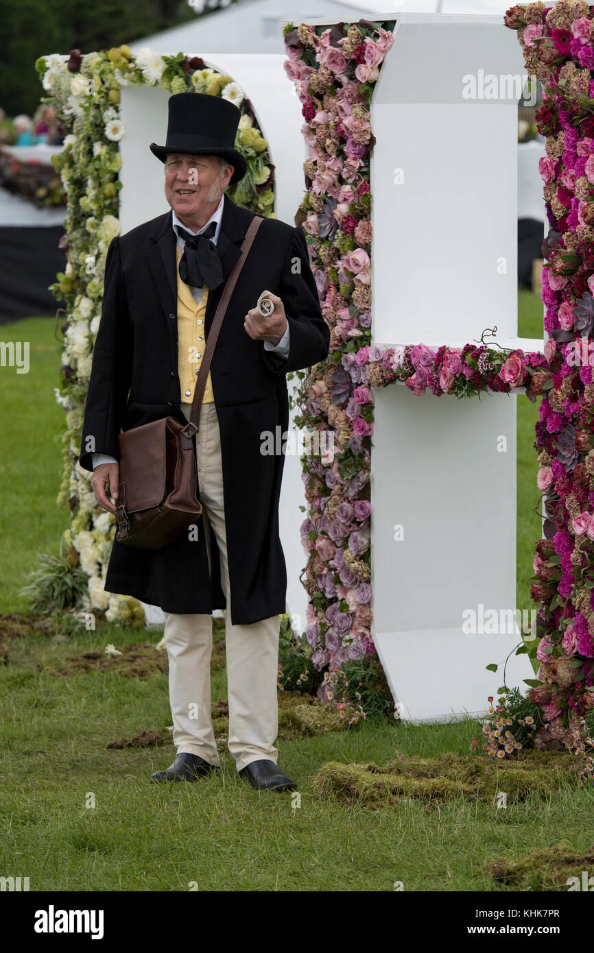 Mann zu sprechen, ist im viktorianischen Outfit & stehend gekleidet mit riesigen Blumen RHS schreiben - RHS Chatsworth Flower Show Showground, Derbyshire, England, UK. Stockfoto