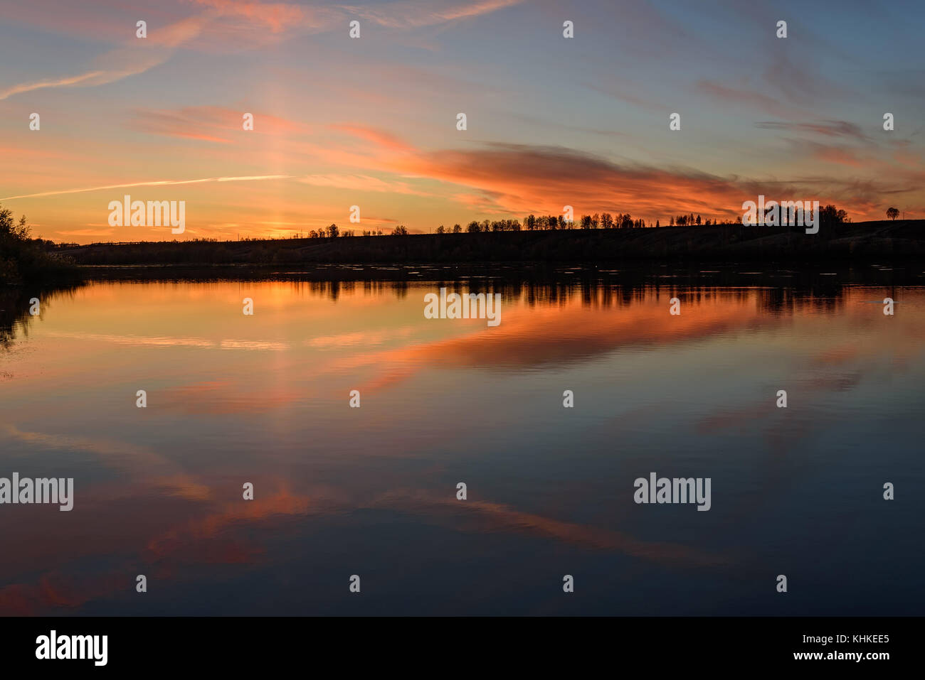 Die malerische orange und braun Sonnenuntergang am See mit wunderschönen zarten Wolken im Wasser widerspiegelt Stockfoto