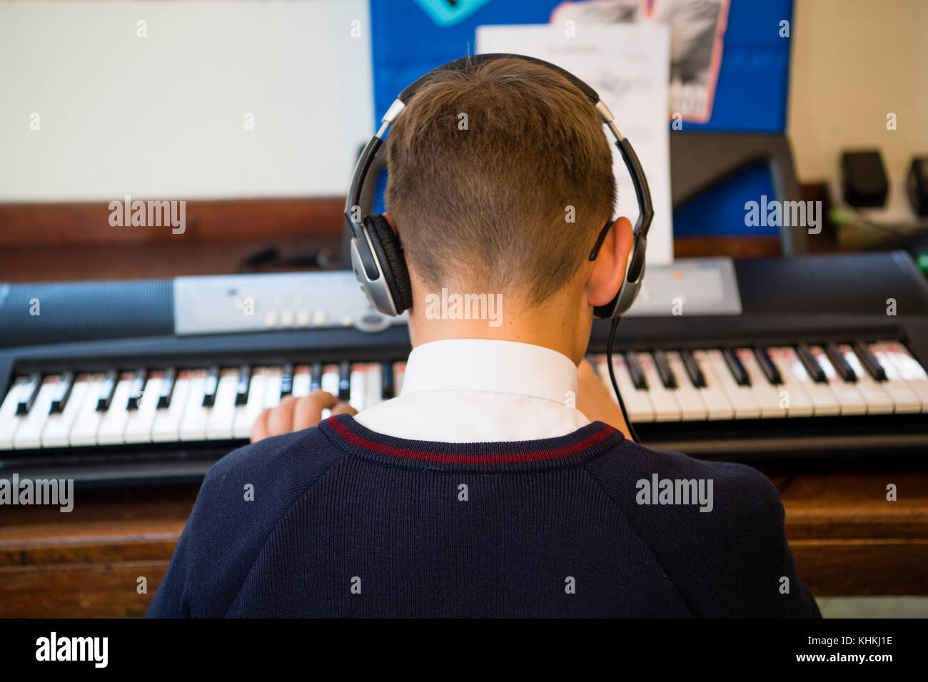 Sekundarstufe in Großbritannien: Rückansicht eines männlichen jungen Schüler mit Kopfhörern Spielen des Keyboards in eine musikstunde Klasse Stockfoto