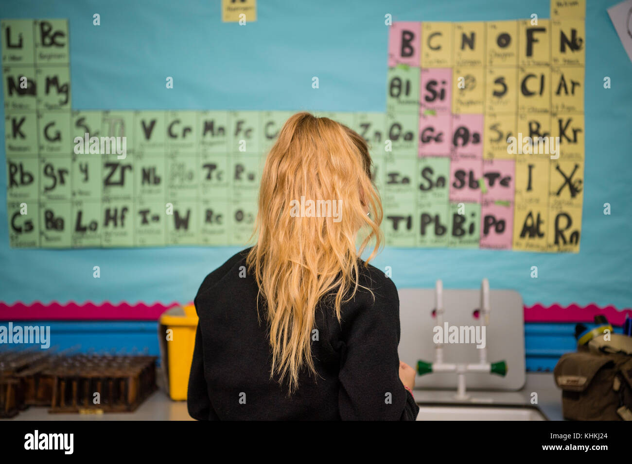 Sekundarstufe in Großbritannien: Rückansicht eines Ein teenager-giirl weiblichen Schüler Student vor dem Element Periodensystem an der Wand in einem Chemie Wissenschaft Lektion Klasse Stockfoto