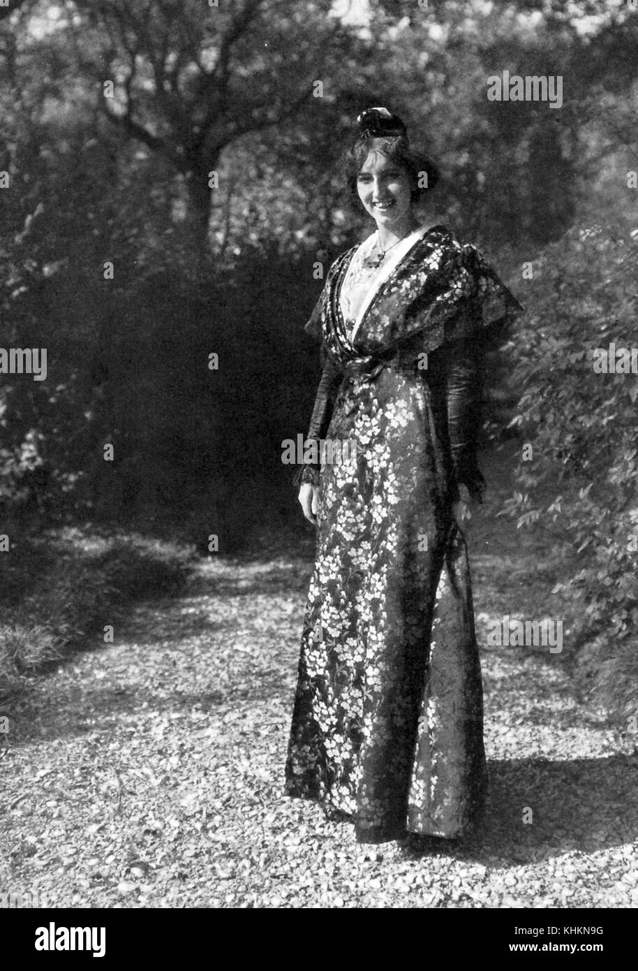 Ein ganzlanges fotografisches Porträt einer lächelnden Frau, sie posiert auf einem Weg in einem Waldgebiet, sie trägt ein traditionelles Kleid von Arlesienne oder Frauen aus Arles, das Kleid ist bodenlang mit langen Ärmeln und verfügt über einen Blumendruck, der im Sonnenlicht leuchtet, Camargue, Frankreich, Juli 1922. Stockfoto