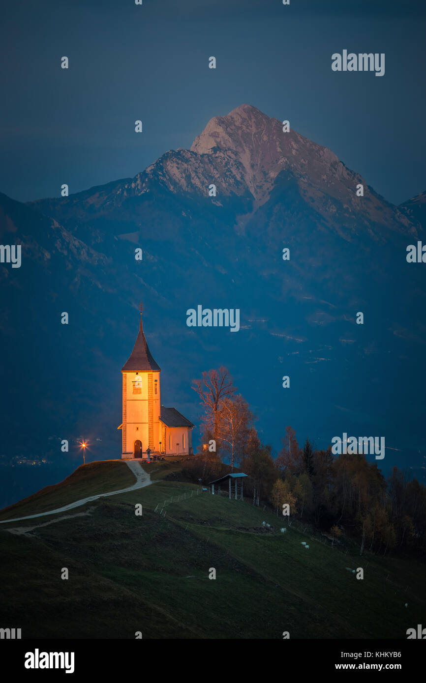 Jamnik, Slowenien - Schöne beleuchtete St. Primoz Bergkirche mit Julischen Alpen im Hintergrund zu blauer Stunde Stockfoto