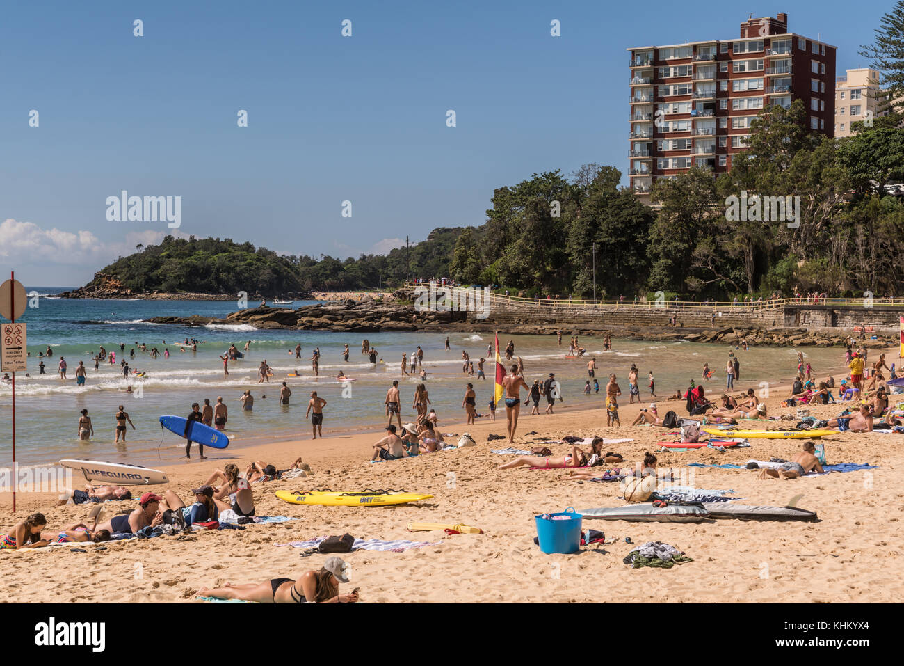 Sydney, Australien - 26. März 2017: Abschnitt des Manly Beach mit Sand und Tasmansee. Menschen auf dem Sand und im Wasser. Wohnungsturm und grün Stockfoto