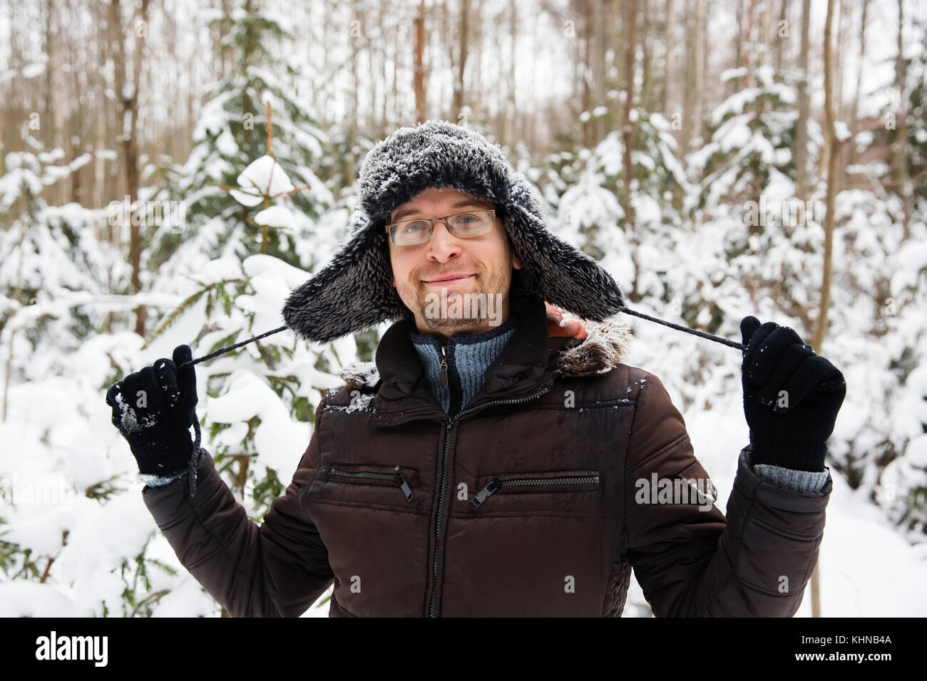 Mann in Fell winter Mütze mit Ohrenklappen lächelnd Portrait. extreme im Wald Stockfoto