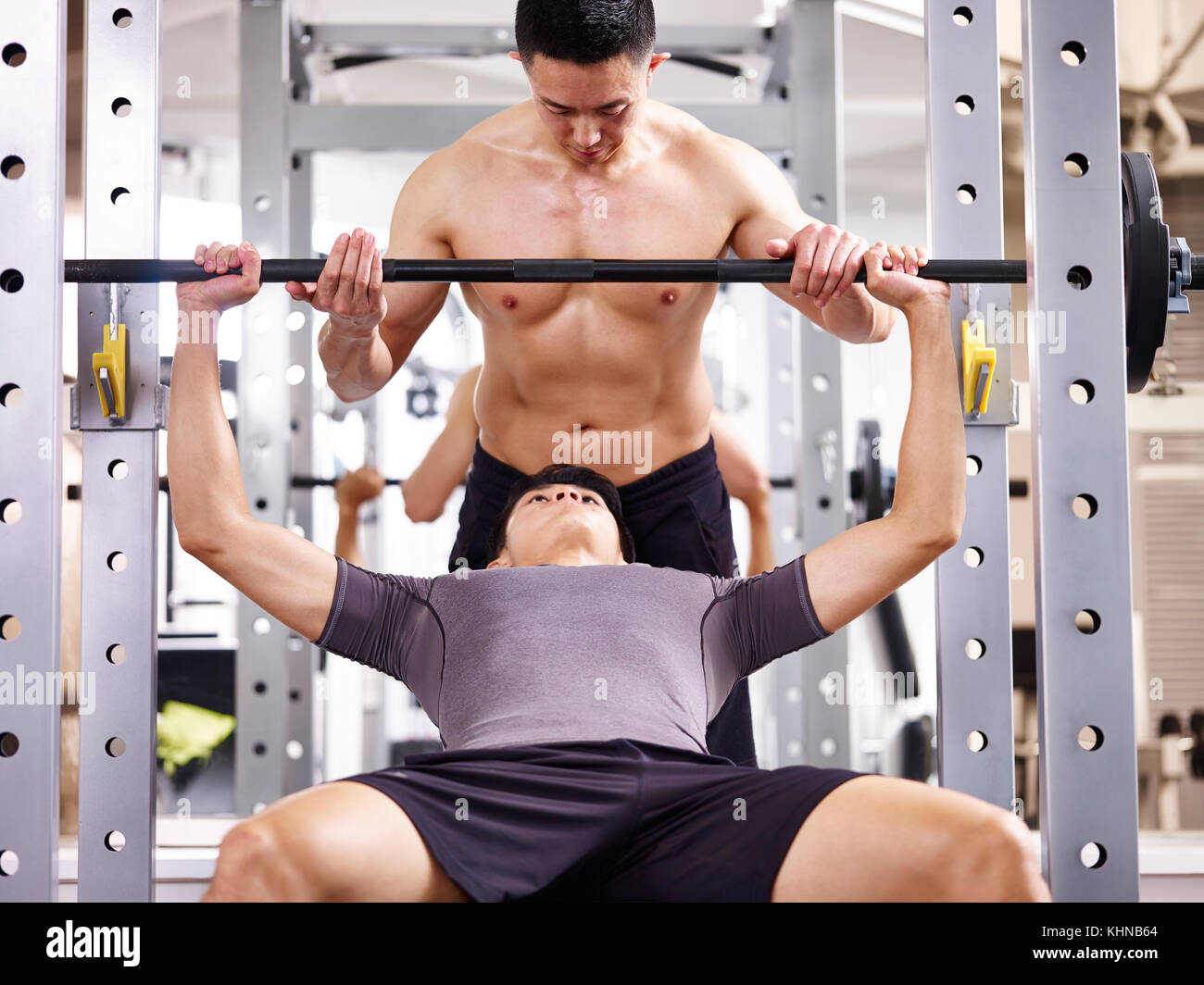 Jungen asiatischen Menschen durch Trainer trainiert und heben das Gewicht in der Turnhalle. Stockfoto