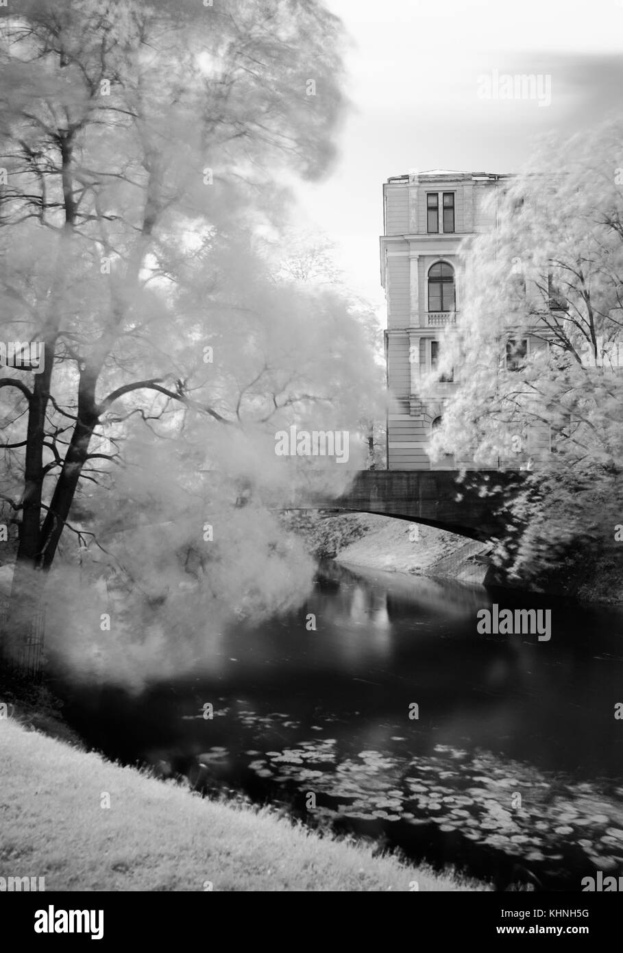 Eine schwarzweiß-IR-Filter Umwandlung einer Szene in einem Park mit einer Brücke über einen Kanal, Bäume mit weichen Bewegung in den Niederlassungen und ein altes Gebäude. Stockfoto