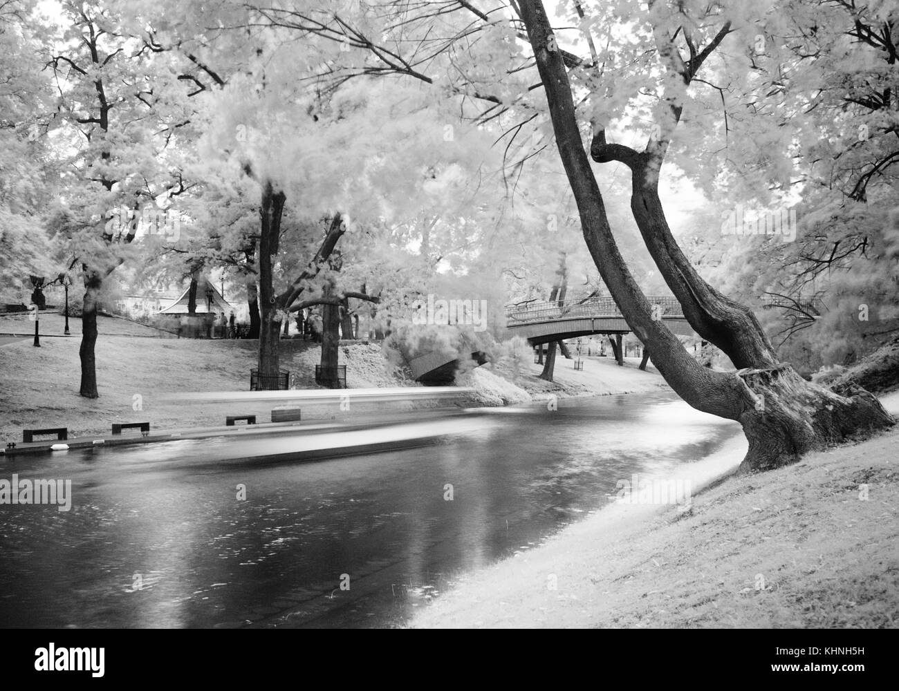 Ein Schwarzweiß-Foto von einem Park in Riga mit einem Boot vorbei rutscht auf einem Kanal mit schönen Bäumen auf beiden Seiten. Stockfoto