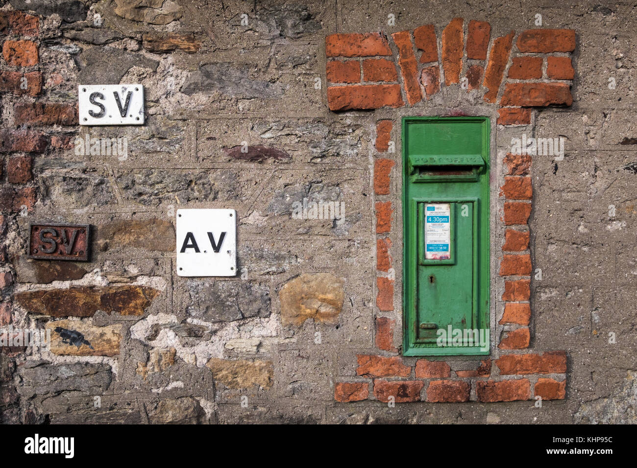 Grüne Post Box für den Versand von Briefen, in einem roten Backsteingebäude aus dem Rahmen in einer Mauer aus Stein mit SV und AV-metall Plaketten, Waterford, Irland Stockfoto