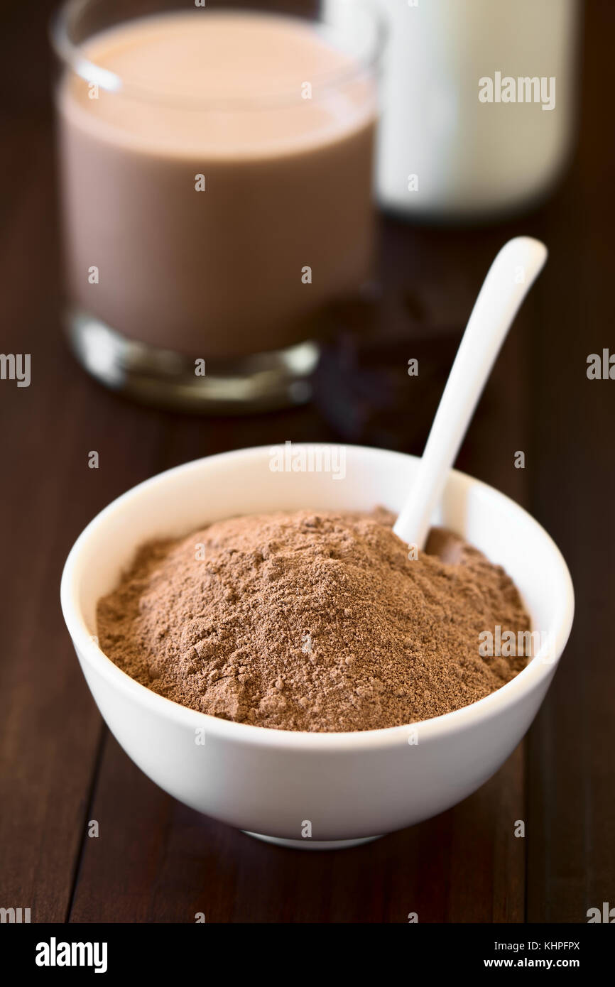 Kakao oder Schokolade Drink Pulver in Schale mit Löffel, Schokolade und Milch in den Rücken, fotografiert mit Tageslicht (selektive Fokus) Stockfoto