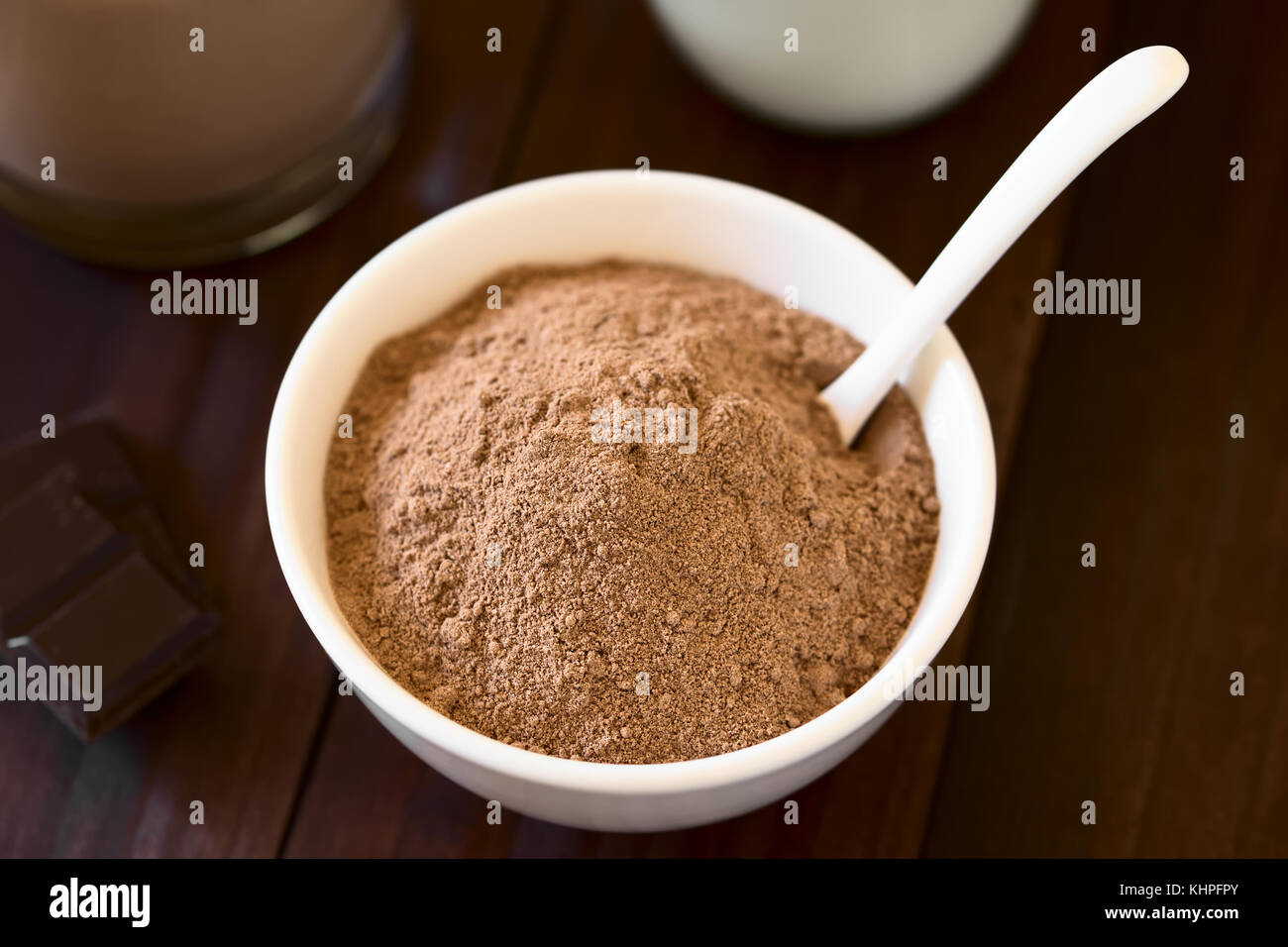 Kakao oder Schokolade Drink Pulver in Schale mit Löffel, Schokolade und Milch in den Rücken, fotografiert mit Tageslicht (selektive Fokus) Stockfoto