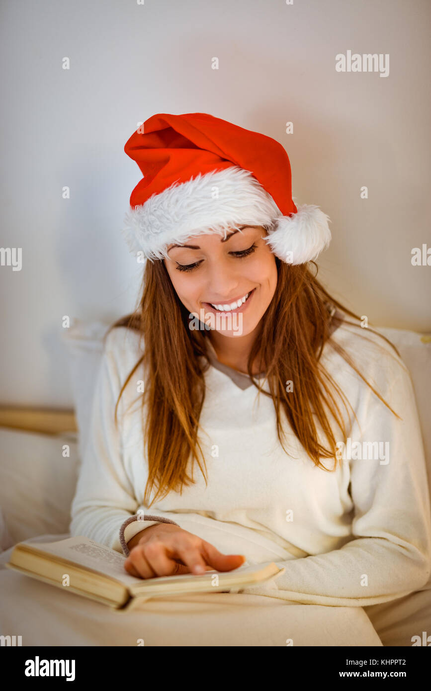 Schöne lächelnde Mädchen mit weihnachtsmütze Entspannen in gemütlichen Bett und Lesen Buch. Stockfoto