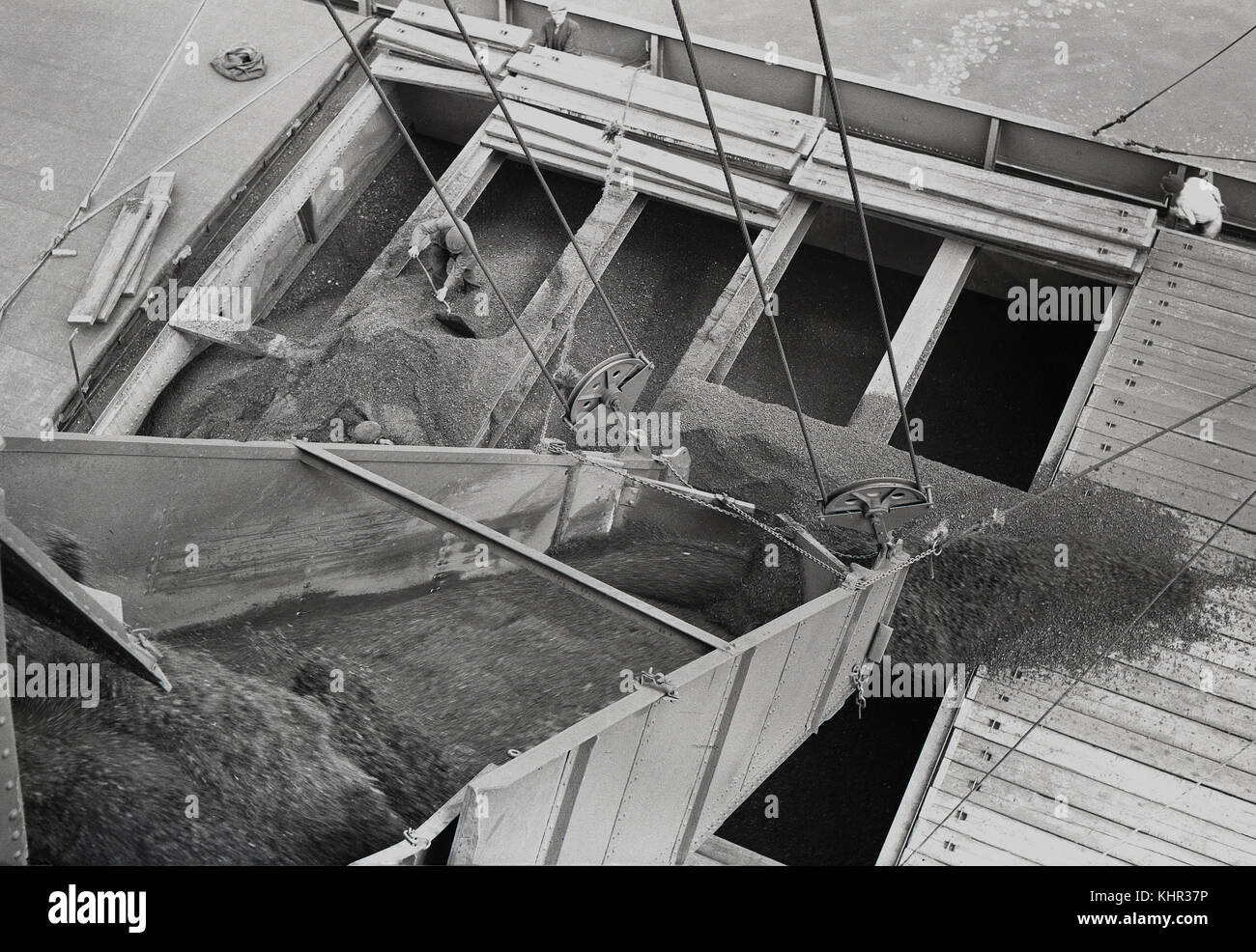 1950er Jahre, historisches Bild, das eine Ladung industrieller Rohstoffe zeigt, die einen shute in den Schiffsrumpf oder den Laderaum eines Schiffes an Londoner Docks hinunterfährt, ein männlicher Arbeiter, der den Überlauf mit einem Spaten bewegt, England, Großbritannien. Stockfoto