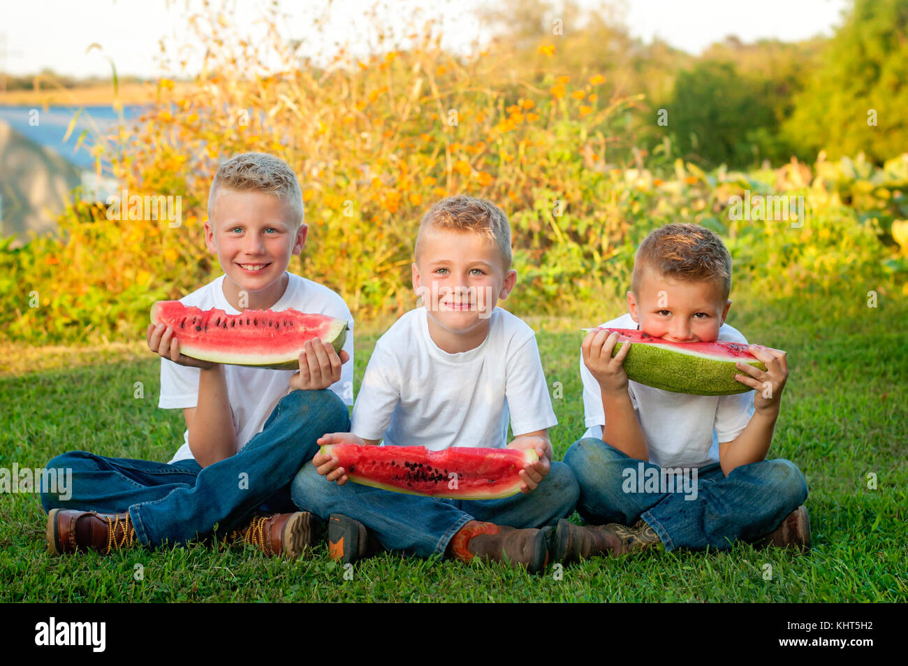 Drei Brüder essen große Scheiben Wassermelone auf dem Bauernhof Stockfoto