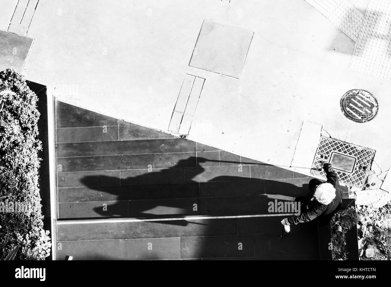 Alte Frau auf der Straße sitzen und ihre großen Schatten Stockfoto
