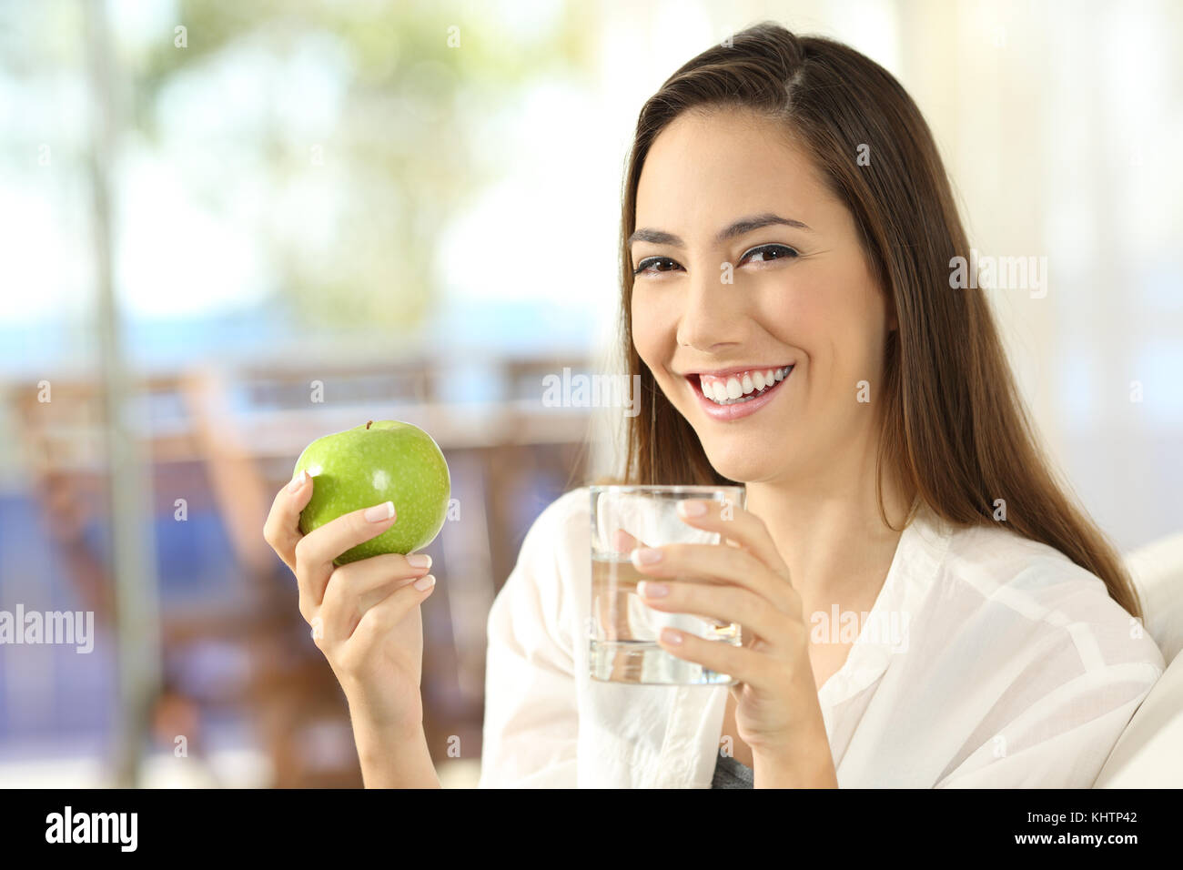 Glückliche Frau mit einem Apfel und einem Glas Wasser sitzen auf einem Sofa im Wohnzimmer zu Hause Stockfoto